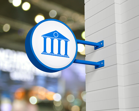 Bank icon on hanging blue rounded signboard over blur light and shadow of shopping mall, Business banking online service concept, 3D rendering