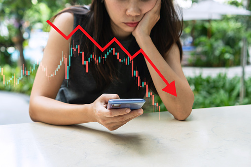 Stressed Asian businesswoman crypto trader broker investor look at the mobile phone analyzing stock exchange market crypto trading decreasing chart data fall down. Stock market concept. Copy space