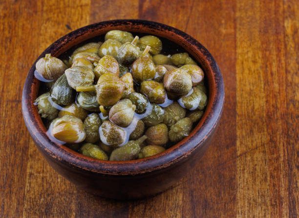 istock Clay bowl with capers stands on a wooden table. 1435774763