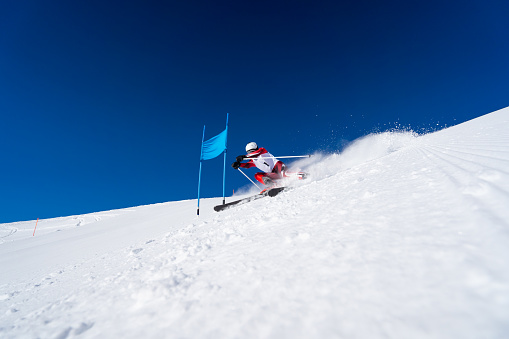 Wide angle view low perspective dynamic aggressive focused professional ski racer skiing giant slalom on sunny winter day with clear blue sky