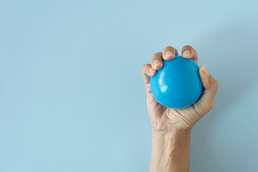 woman hand holding stress ball on blue table background, stress or sport exercise concept