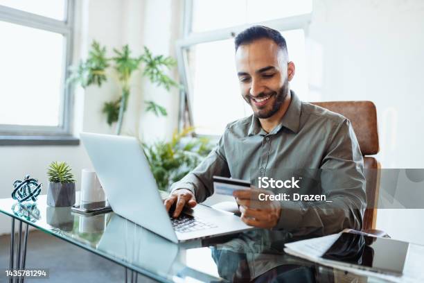 Mid Adult Smiling Latin Businessman In Office Using Credit Card To Pay Online Stock Photo - Download Image Now
