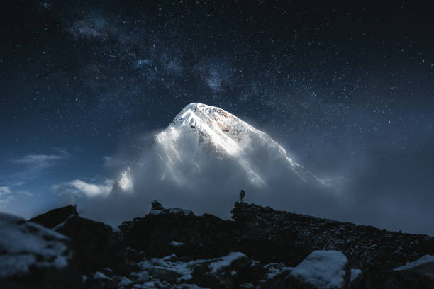 отважный одинокий горный путешественник стоит перед огромной заснеженной горой и звездным небом. профессиональный турист на вершине гор с - trail ride стоковые фото и изображения