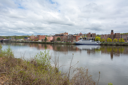 Troy, New York, United States of America - April 26, 2017. View of downtown Troy across the Hudson River. View with buildings and a sailing boat on a cloudy spring day.