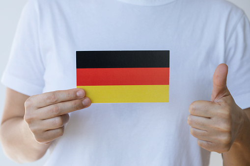 Hand is showing German flag to camera and is doing thumbs up gesture.