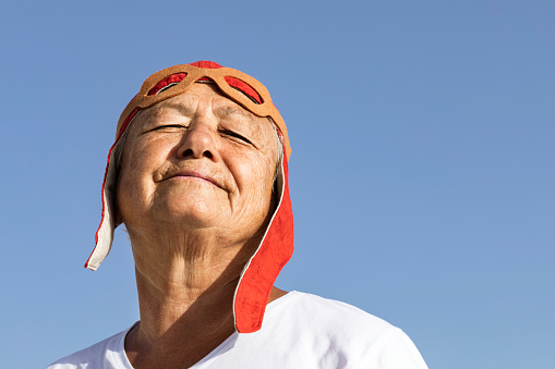 Close up of a senior woman wearing retro style pilot costume. She is looking up while she is daydreaming. Representing active senior adult concept.