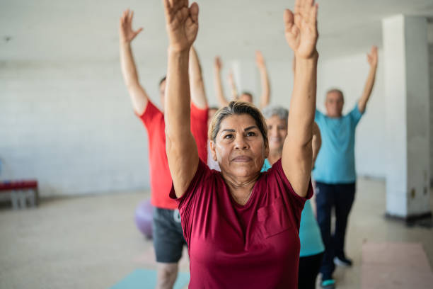 mujer mayor estirándose con compañeros de clase en el estudio de yoga - relaxation yoga adult balance fotografías e imágenes de stock