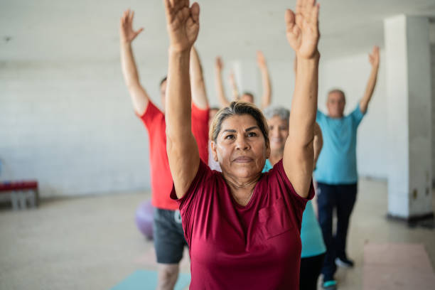 donna senior che fa stretching con i compagni di classe nello studio di yoga - relaxation yoga adult balance foto e immagini stock