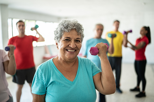 Portrait of senior woman lifting weights with classmates at the gym