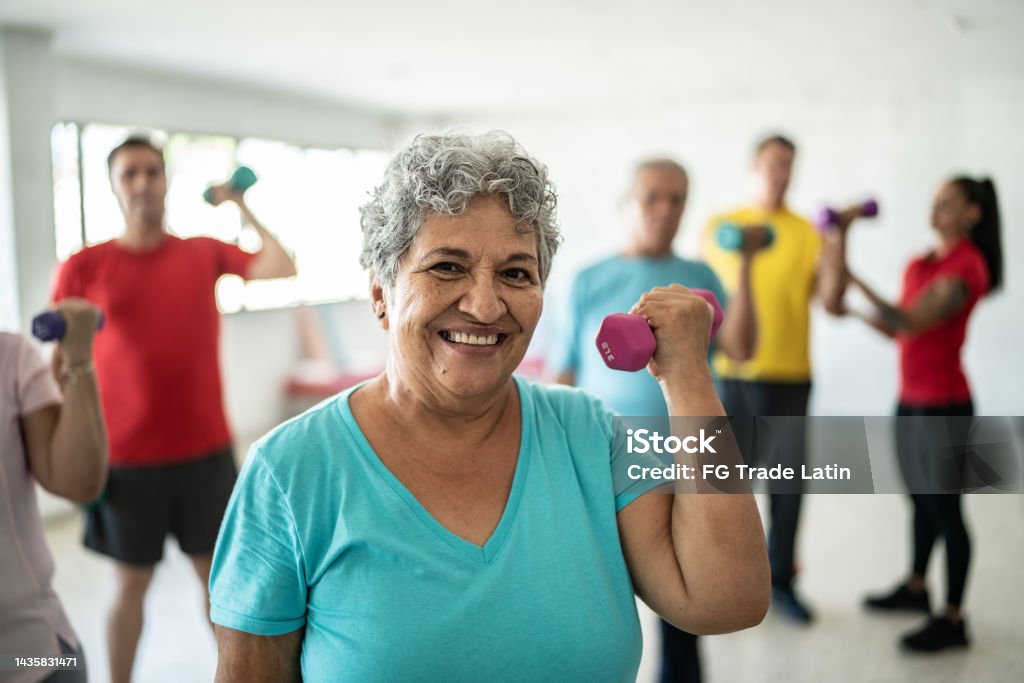 Portrait of senior woman lifting weights with classmates at the gym Senior Adult Stock Photo