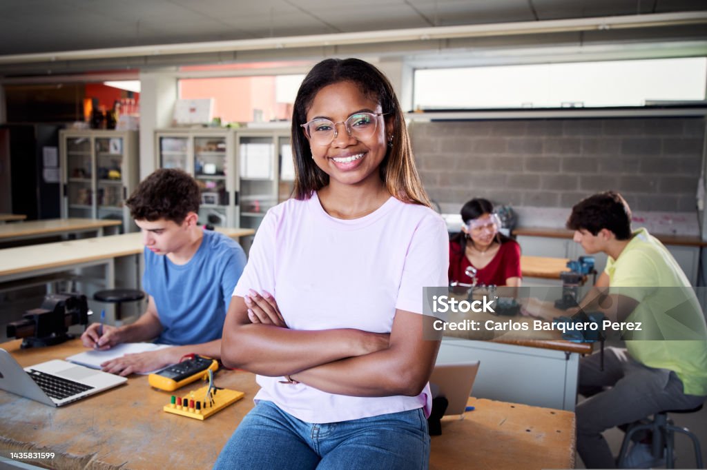 Portrait of a latina in the classroom looking at the camera with her arms crossed. Young students doing technical vocational practice in electronic class, Concept of education and technology. Portrait of a latina in the classroom looking at the camera with her arms crossed. Young students doing technical vocational practice electronic class, Concept of education and technology High quality 20-29 Years Stock Photo