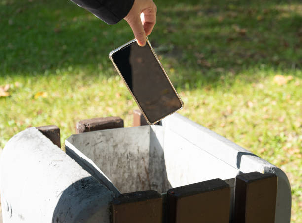 Hand throws out smartphone. Throwing electronic device into street trash can, throwed away smartphone, dangerous garbage concept, blurred background