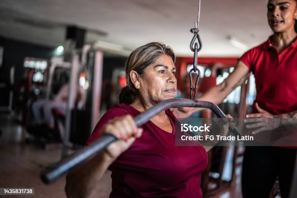 Senior Woman Pulling Weight Machine With Help Of Fitness Trainer At The Gym Stock Photo - Download Image Now