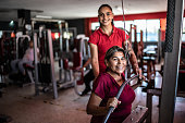 Portrait of senior woman with fitness instructor pulling weight machine at the gym