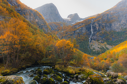 Scenic view of the beautiful waterfall falling from the glacier, surrounded by the mountains and the yellow fall woodland in Jostedalbreen National park, Western Norway