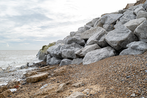 Recently dumped large granite boulders along a beach to help with sea defences from costal erosion. Recent landslides have meant houses are in danger of collapsing.