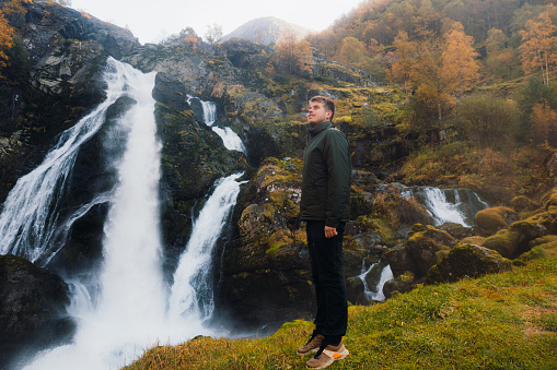 A man explorer in jacket overlooking the yellow forest and the waterfall in Jostedalbreen National park, Western Norway