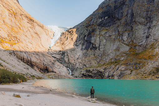 Silhouette of a man in a jacket staying by the lakeshore overlooking the crystal blue glacial lake in Jostedalbreen National park, Western Norway