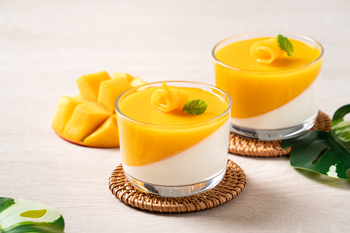 Delicious double colored mango panna cotta mousse pudding with diced mango pulp flesh topping on wooden table background.