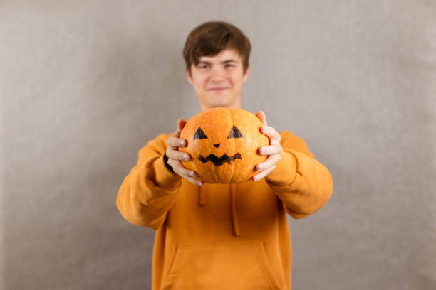 istock A cute young feather in an orange jumper pulls a Halloween pumpkin on his outstretched arms, a place for text 1435848809
