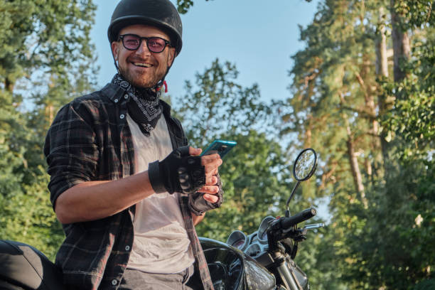 istock Young male biker in helmet using mobile phone and smiling sitting on a motorcycle 1435852665