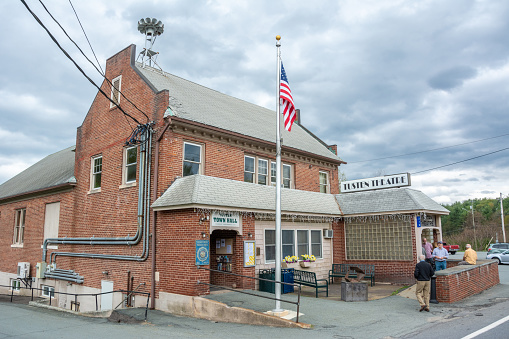 Narrowsburg, New York, United States of America - April 29, 2017. Building of Tusten Theatre and Tusten Town Hall at 210 Bridge Street in Narrowsburg, NY. Built in 1926 by the Narrowsburg firemen, it was originally called the Community Hall and used as a dance and banquet facility. In the 1930s, Harvey English, a theatre chain owner from Hancock, NY, converted the dance hall into a sloped floor movie house. After the conversion, English leased the space from the firemen and ran a commercial movie operation, the Park Theater, for a number of years. The movie business was bought out, changed hands a few times, and then closed permanently in 1985. In the meantime, the firemen sold the building to the Town of Tusten for use as a town hall. In the fall of 1987, the Town of Tusten and the Delaware Valley Arts Alliance (DVAA) negotiated a lease that would give management of the theatre portion of the building to DVAA. They renamed the space Tusten Theatre. View with people.