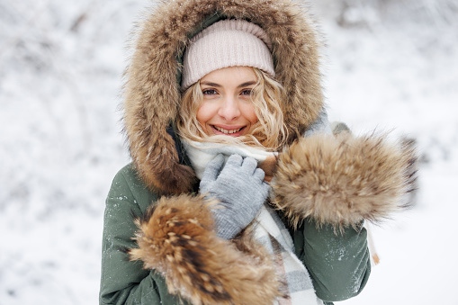 Portrait of beautiful young woman in warm clothes in winter forest