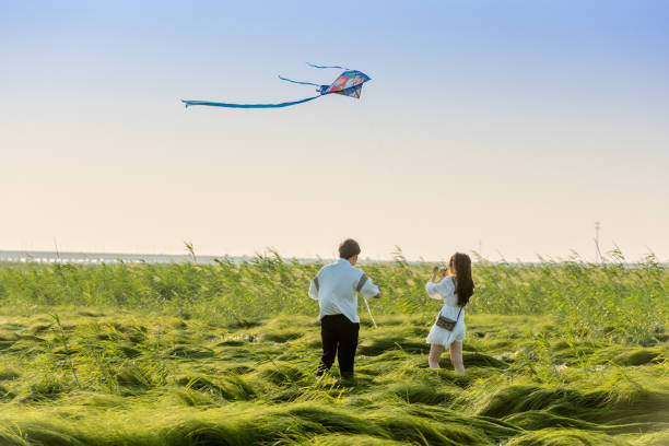 A helping hand. Caring mother teaches little girl to fly a kite in autumn nature at sunset. Child development, learning, freedom, joy, & connecting with nature.