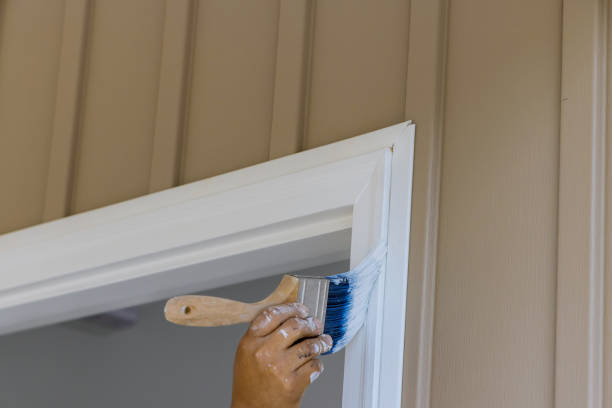 Using a paintbrush, a carpenter works on painting wooden moldings and door trims stock photo