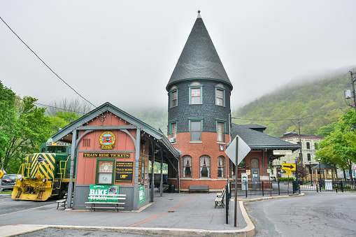 Jim Thorpe, Pennsylvania, United States of America - May 1, 2017. Central Railroad of New Jersey Station, now owned by Lehigh Gorge Scenic Railway, in Jim Thorpe, PA. It was designed by Wilson Brothers & Company of Philadelphia, Pennsylvania, and built in 1888 by the Central Railroad of New Jersey. It is a 1 1/2-story, five bay, red brick building in the Queen Anne style. It features a 3 1/2-story, cylindrical corner tower with a cylindrical roof. It is owned by the Lehigh Gorge Scenic Railway and served as a visitor center. View on a foggy spring day.