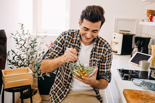 Happy young man eating a healthy salad for breakfast