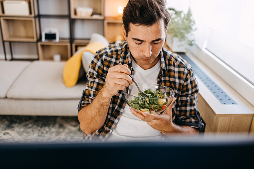 Man eating vegetable salad at computer