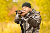 Selective focus of the hands of a man in a camouflage protective suit who loads a double-barreled shotgun. The concept of hunting.