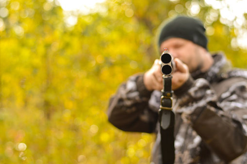 Selective focus of the hands of a man in a camouflage protective suit who loads a double-barreled shotgun. The concept of hunting.