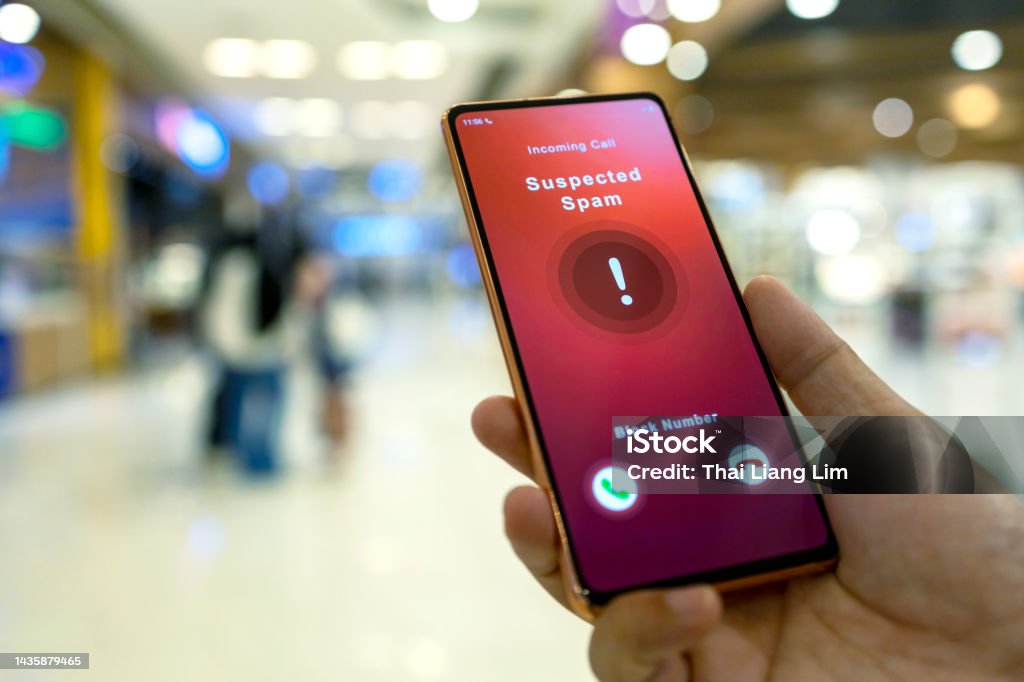 Person receiving suspected spam call on smartphone from an unknown caller in a shopping mall A man receiving an incoming suspected spam call on her phone. The network provider detect the scam and show warning sign to rejects the call. High angle view. White Collar Crime Stock Photo