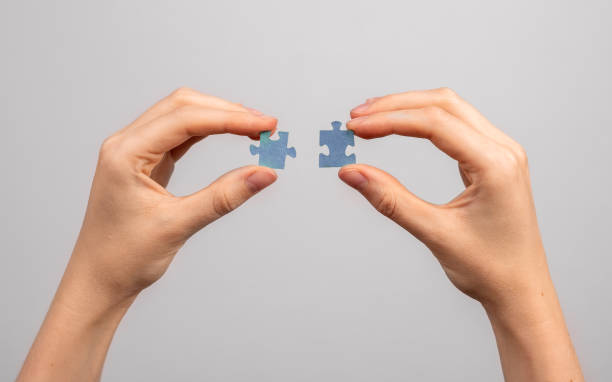 istock Hands connecting two jigsaw puzzle pieces closeup. Merger, business connection, assembly concept 1435879817