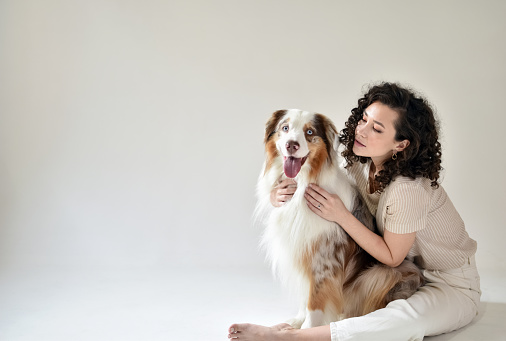 Wonderful curly female model in the studio with a dog. Indoor portrait of a girl enjoying a photo session with her cute pet Australian Shepherd dog