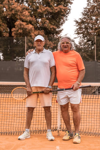 portrait of two senior tennis players dressed in sportswear relaxing at the end of the game on a clay tennis court stock photo