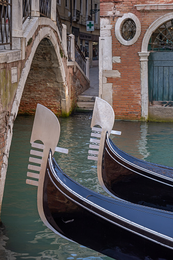 Bows of two gondolas with a classic Venetian bridge in the background and out of focus