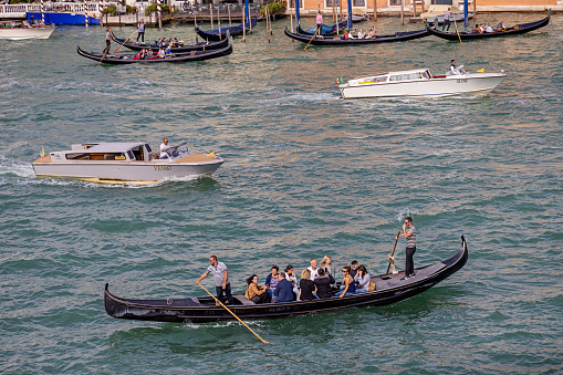 Venice, Italy - October 9th 2022:  Large group of people being ferried across the Canal Grande by two gondoliers and surrounded by motorboats, probably water taxis