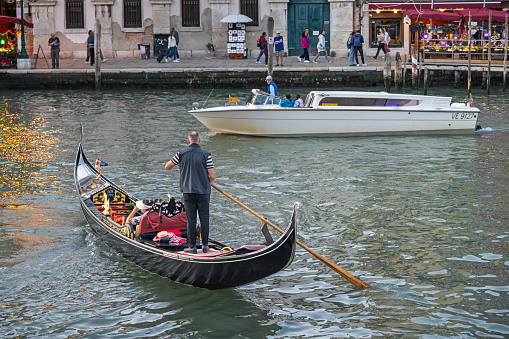 Venice, Italy - October 8th 2022:  Motorboat, probably a water taxi, crossing the path of a gondola with tourists in Canal Grande in the center of Venice