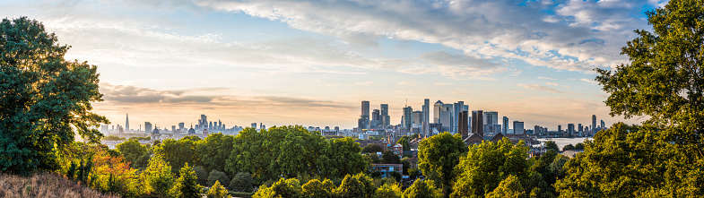 Panoramic view across the trees of Greenwich Park to the high-rise cityscape of Canary Wharf Docklands and the distant skyscrapers of the City of London.