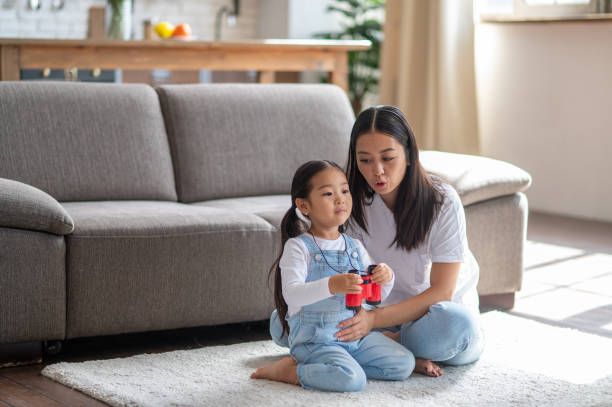 Mother communicating with her child seated on the rug Young female parent talking to a cute little girl with the binoculars in her hands asian mother talking to child stock pictures, royalty-free photos & images