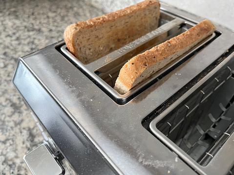 electric toaster on black countertop at home kitchen with white wall and female hand put slice bread for making crispy toast for breakfast, cooking concept