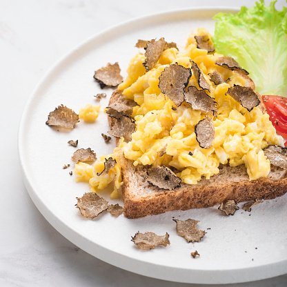 Scrambled eggs recipe with black truffles, bread tomatoes , white background. Black truffles gourmet brunch, breakfast. Healthy recipe of Piedmont, Italy, Spain and France, square crop