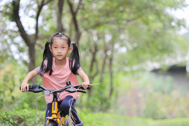Happy siblings - girl and boy ride bicycles in forest.