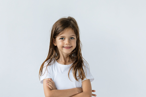 Caucasian little girl wearing white t-shirt is looking at camera with a cute smile in front of white background.