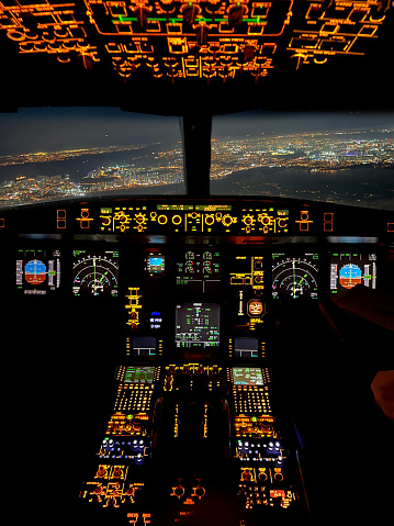 cockpit point of view control pannel of airplane at night and city lights is saw from window horizontal photo