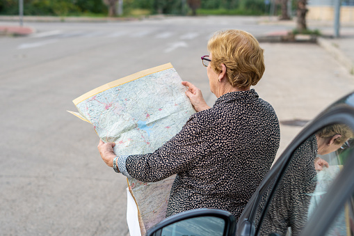 Senior woman looking at a paper map leaning against a car