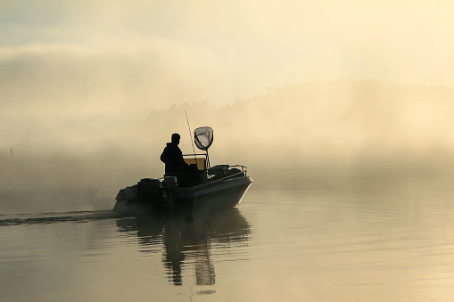 Silhouette of a fisherman in his boat, early in the morning with a lot of fog on the lake.